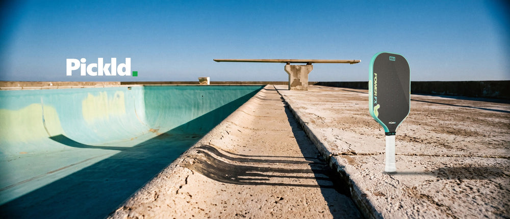 The JOOLA Perseus Power FX standing on the sunlit concrete deck of a drained pool, a springboard on the horizon