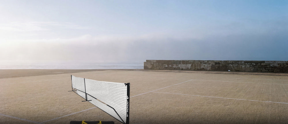 A regulation portable pickleball net standing on a lined hard court at first light