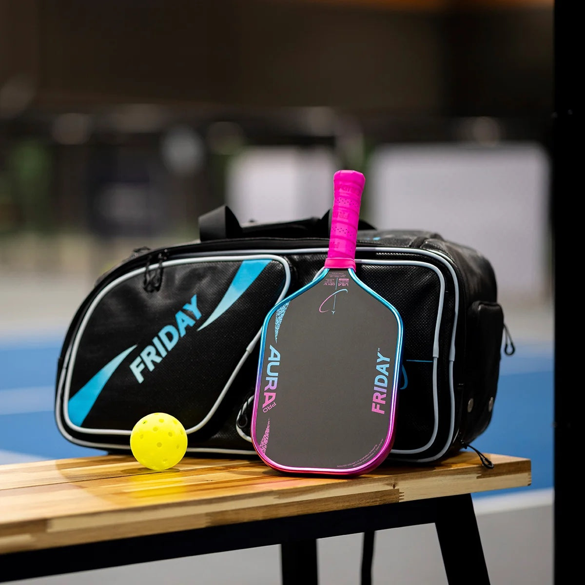 Friday Aura Pro Vice Limited Edition paddle resting against a Friday bag courtside with a pickleball